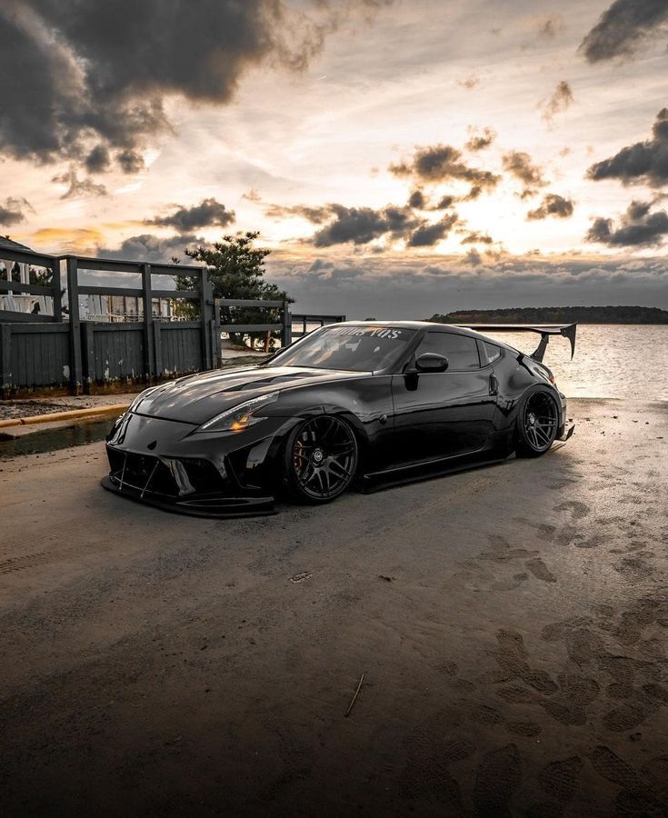 a black sports car parked in front of a body of water with the sun setting behind it