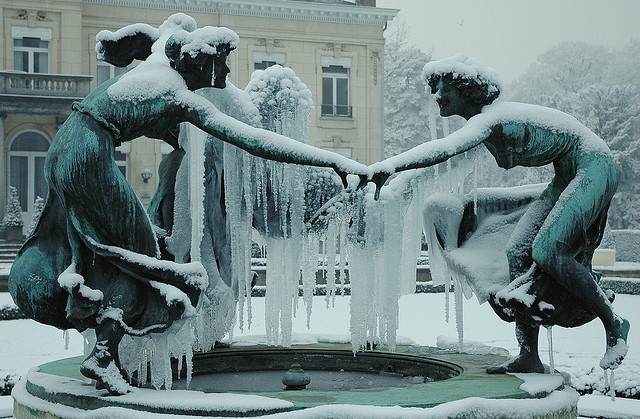 two statues holding hands over a fountain covered in snow