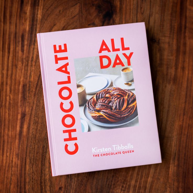 a cookbook with the title chocolate all day written in red and on top of a wooden table