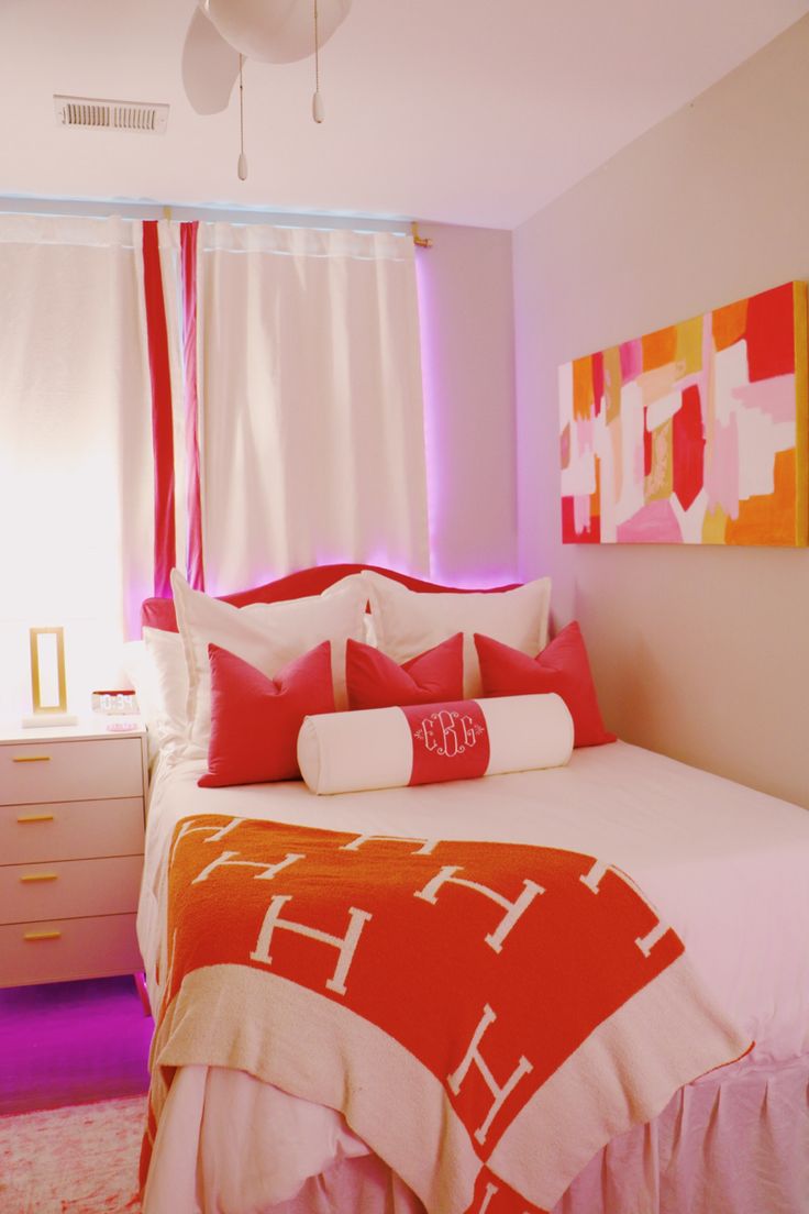 a bed with red and white pillows on top of it next to a window in a bedroom