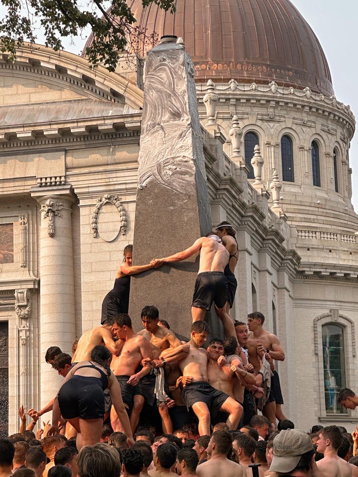 a group of men standing on top of each other in front of a large building