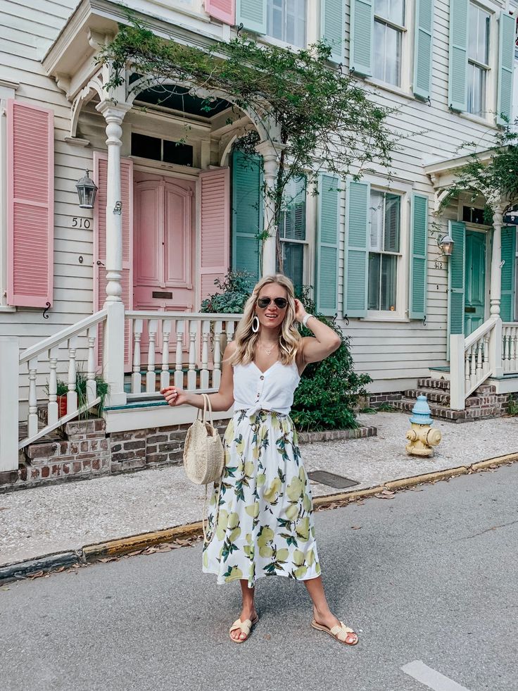 a woman standing in front of a house wearing a white top and floral print skirt