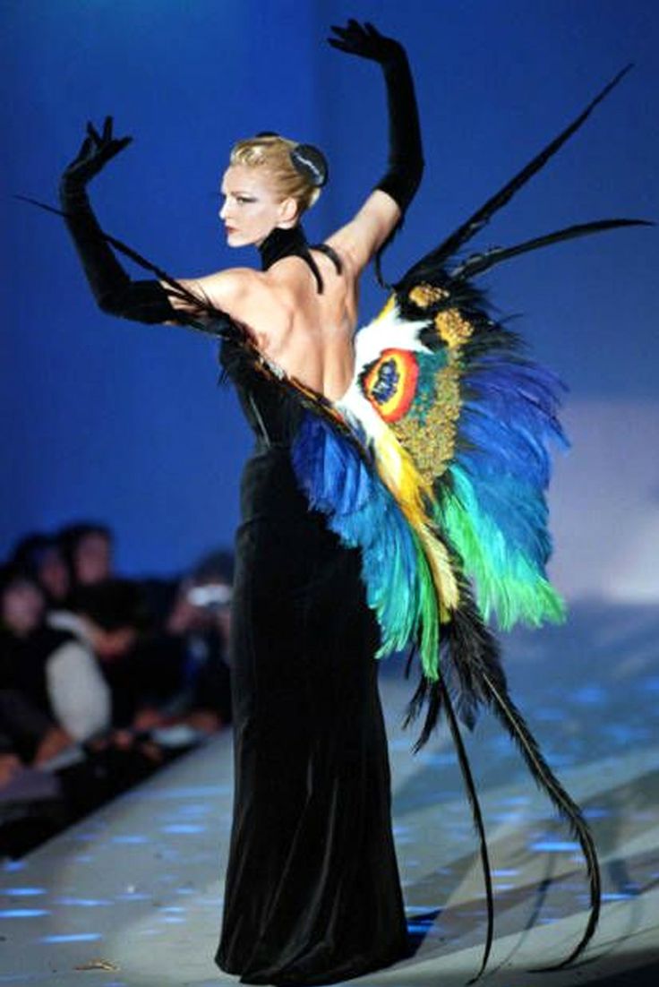 a woman is walking down the runway in a black dress with colorful feathers on it