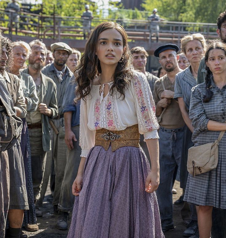 a woman in a long purple dress standing next to a group of men and women