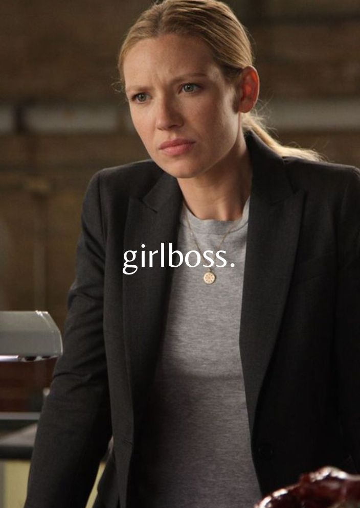 a woman in grey shirt and black blazer looking at the camera with words girlboss on it