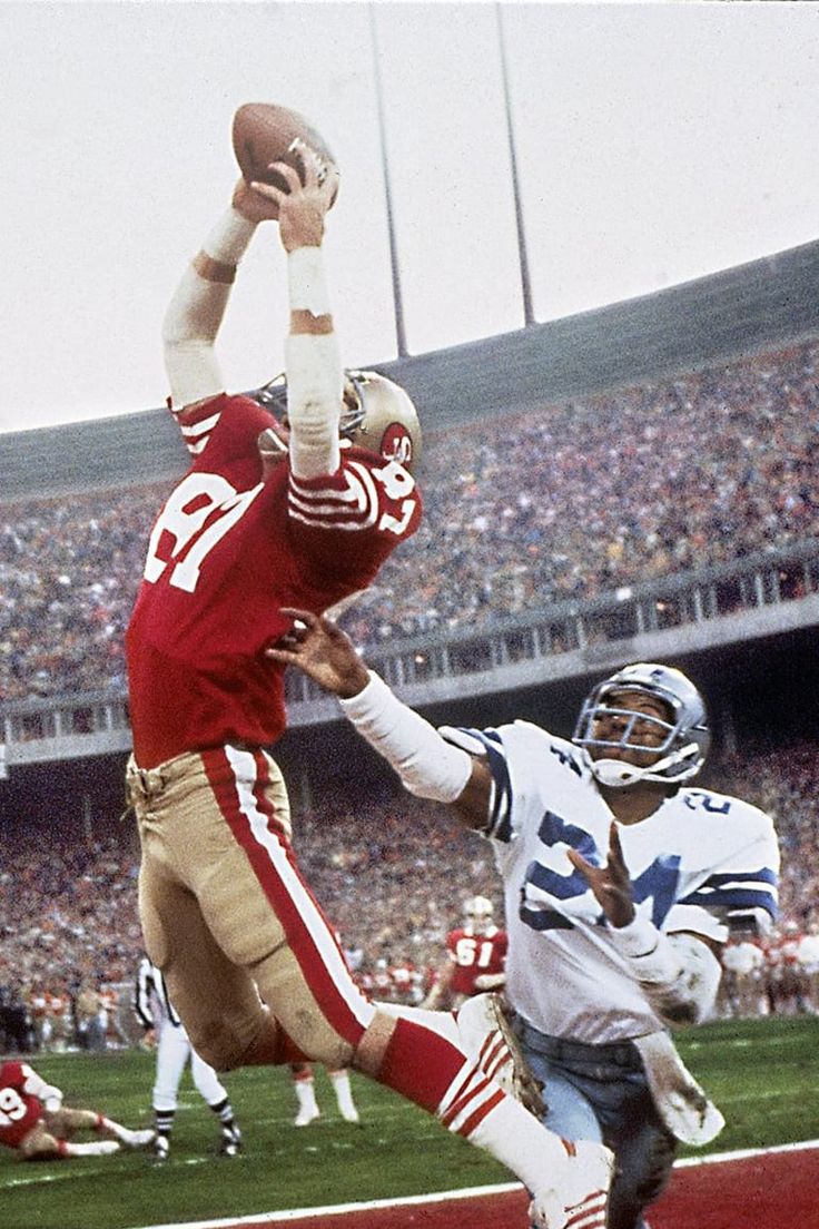 a football player jumping up into the air to catch a ball in front of an opponent