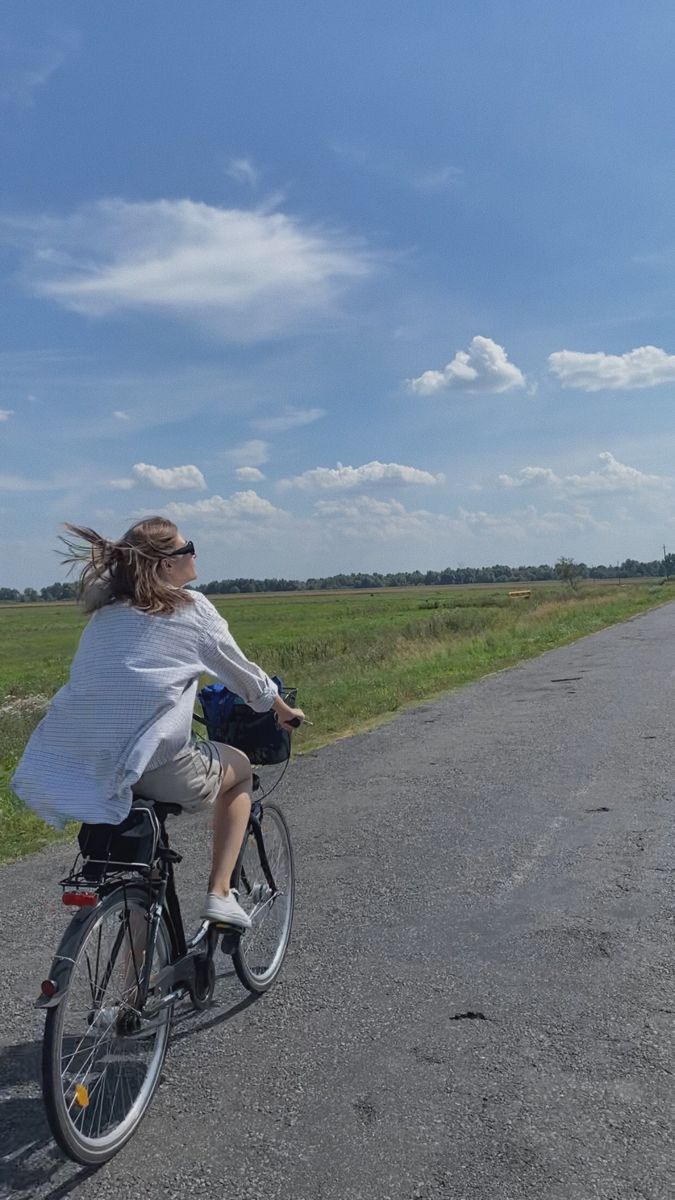 a woman riding her bike down the middle of an empty road on a sunny day