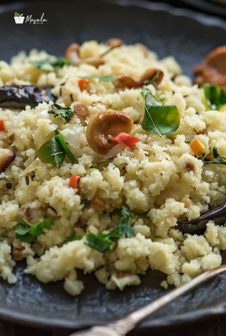 a black plate topped with rice and vegetables next to a fork on top of a table