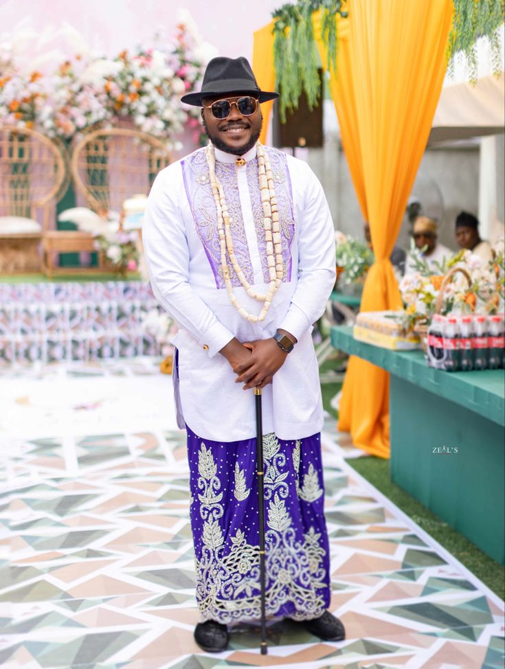 a man in a purple and white outfit standing next to a table filled with flowers