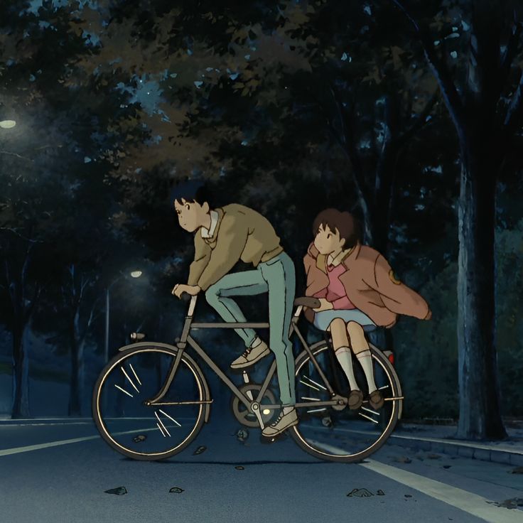 two people riding on the back of a bike in the street at night with trees