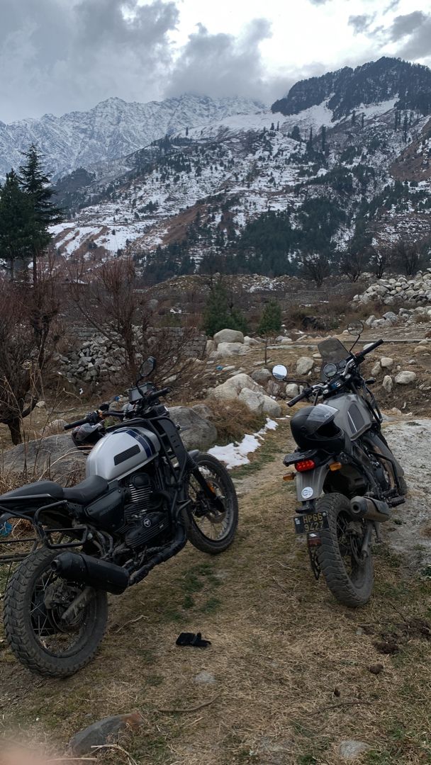 two motorcycles parked next to each other on a field with snow covered mountains in the background