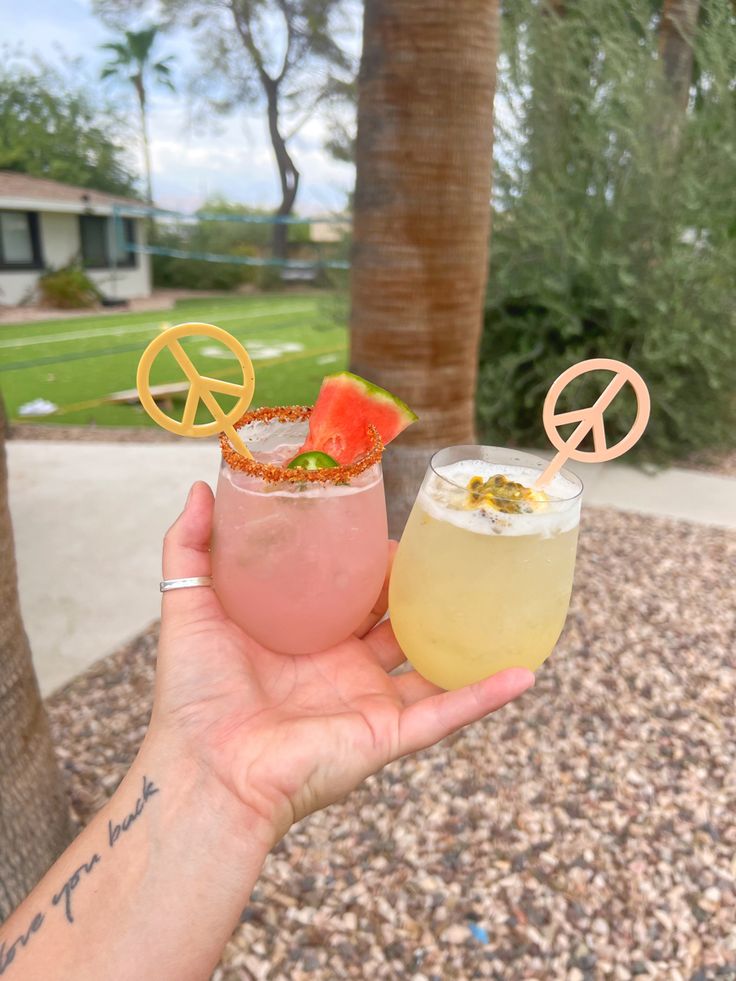 two cocktails are being held up in front of a palm tree with peace signs on it