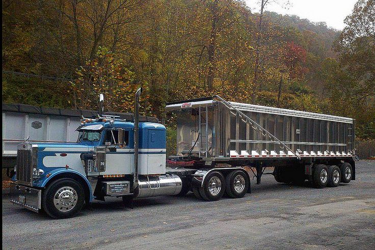 a large semi truck with a trailer attached to it's flatbed is parked in front of a wooded area