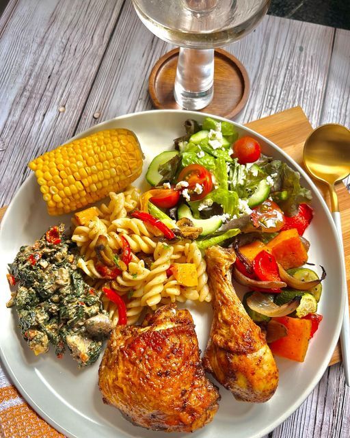 a white plate topped with meat, pasta and veggies next to a glass of wine