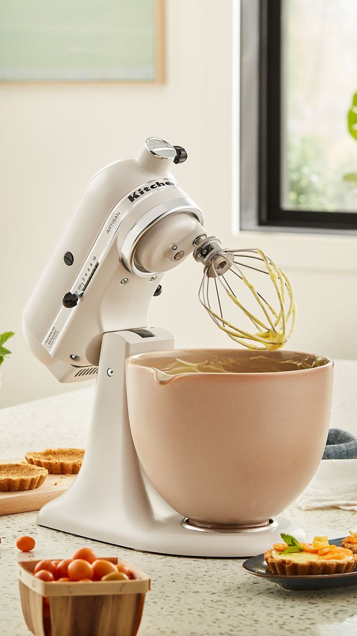 a white mixer with food in it on top of a table next to other bowls