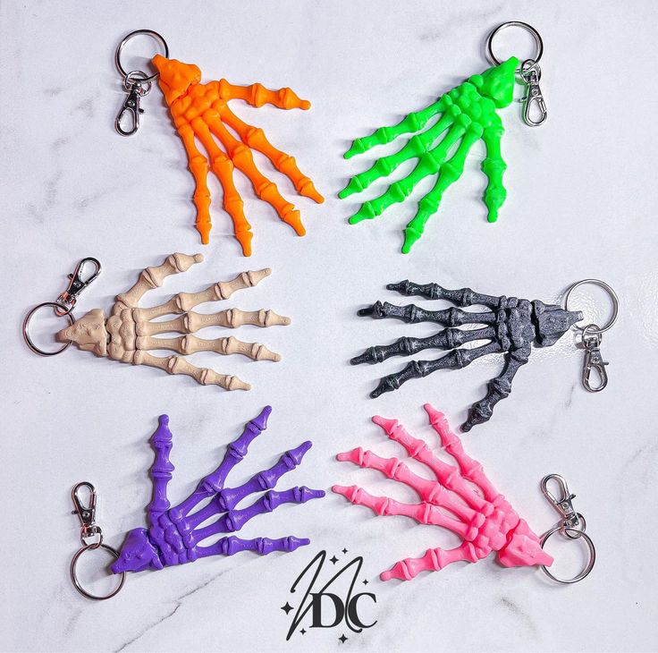 six different colored skeleton hand keychains on a marble surface with the word abc written below them