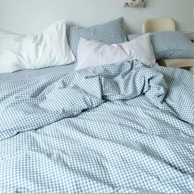 an unmade bed with blue and white checkered comforter, pillows and pillowcases