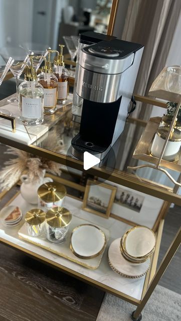 a mirrored table topped with gold and white plates next to a coffee maker on top of a wooden floor