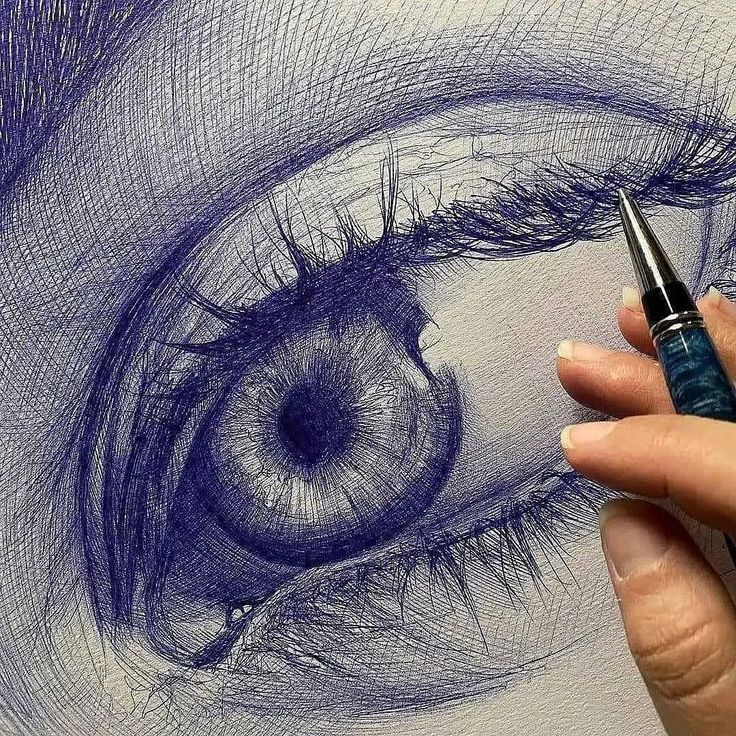 a woman's hand is holding a pen and drawing an eye with blue ink