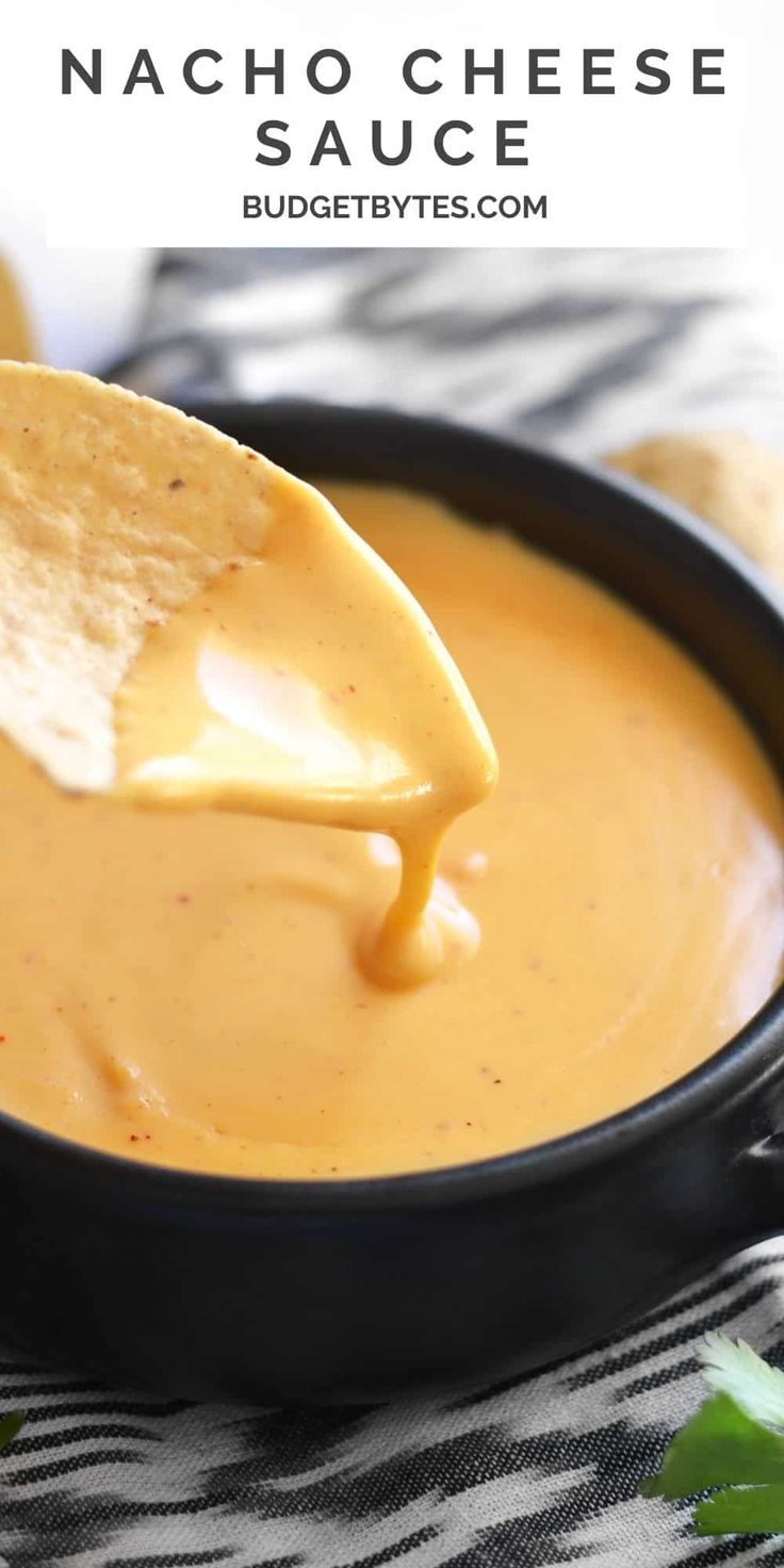 a tortilla chip being dipped with nacho cheese sauce in a black bowl