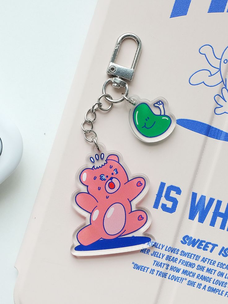 a pink bear keychain sitting on top of a book next to a computer mouse