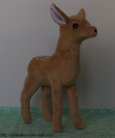 a small stuffed deer standing on top of a green tablecloth covered floor next to a white wall