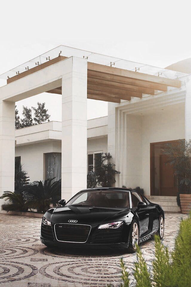 a black sports car is parked in front of a white house with an attached carport