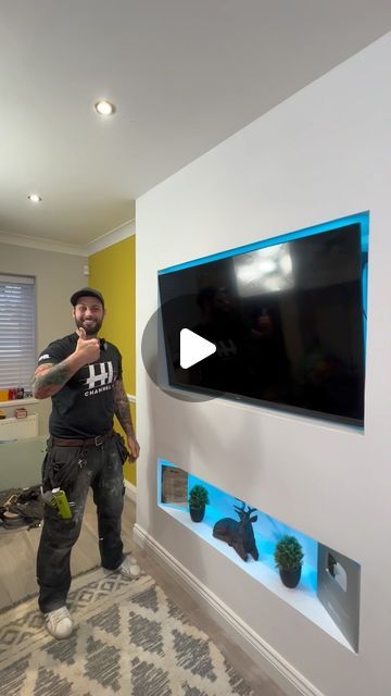 a man standing in front of a flat screen tv next to a wall mounted aquarium