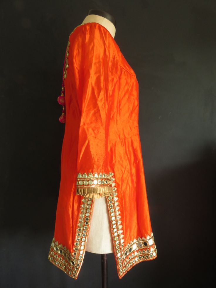 "The embellishment on this stunning outfit is magnificent! It's a very dramatic show-stopper outfit for a special occasion, when you want to make a statement. The mirror-work is made using real mirror glass! Kameez/Top is made of orange silk. The sleeves are not lined and so are somewhat sheer. There is minor staining under the arms. Features: ♦ wire embroidered mirror-work ♦ copper silk pleated ribbon trim ♦ sweetheart neckline trimmed w/ gold metal disc beads and magenta silk piping ♦ high sid Bollywood Anarkali Set With Mirror Work And Traditional Drape, Festive Raw Silk Sharara With Cutdana Details, Orange Kurta With Gota Work In Traditional Drape, Luxury Anarkali Tissue Silk Traditional Wear For Festive, Festive Raw Silk Sharara With Gota Work, Bollywood Style Tissue Silk Kurta For Diwali, Festive Gota Work Sharara In Raw Silk, Bollywood Style Designer Anarkali Set, Navratri Raw Silk Kurta With Mirror Work