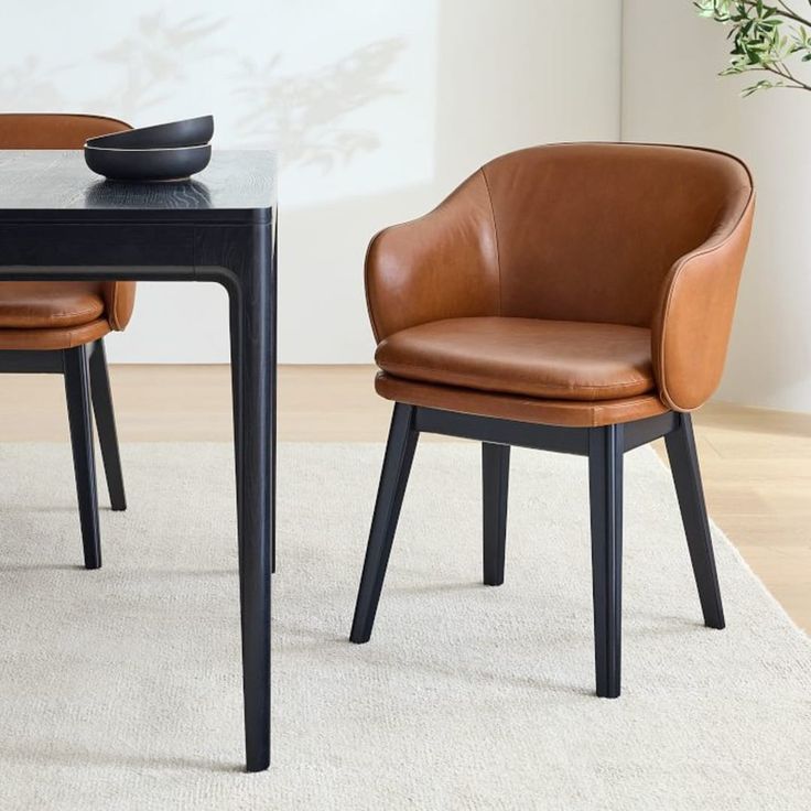 two brown chairs sitting at a black table in front of a vase with flowers on it