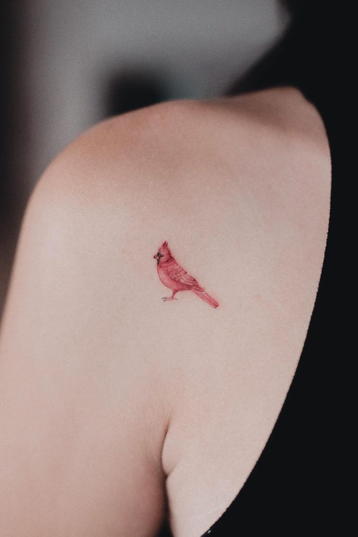 a small red bird tattoo on the back of a woman's upper arm and shoulder