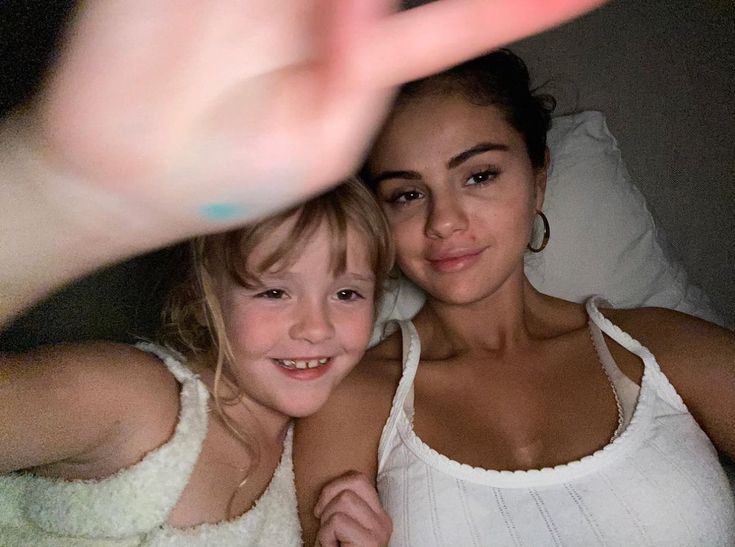 two women in white shirts posing for the camera with one pointing at the camera and the other holding her hand up