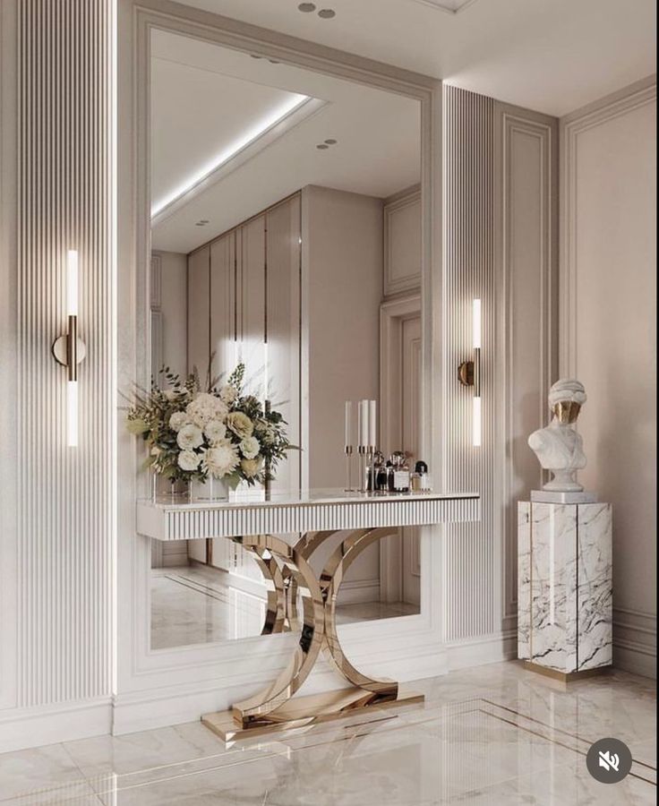 a white marble table with flowers on it in front of a mirror and wall sconces