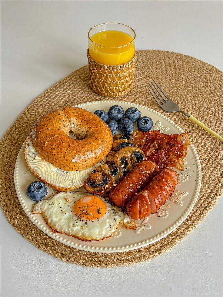 a plate with eggs, sausages, and fruit on it next to a glass of orange juice