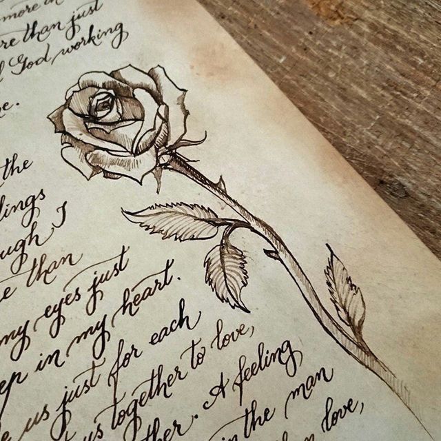 an old book with writing on it and a rose in the middle, sitting on a wooden table