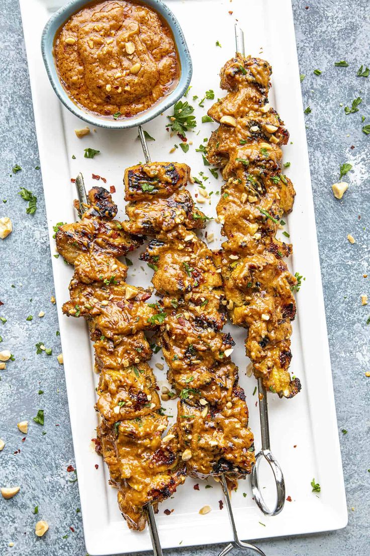 grilled chicken skewers on a white plate next to a bowl of sauce