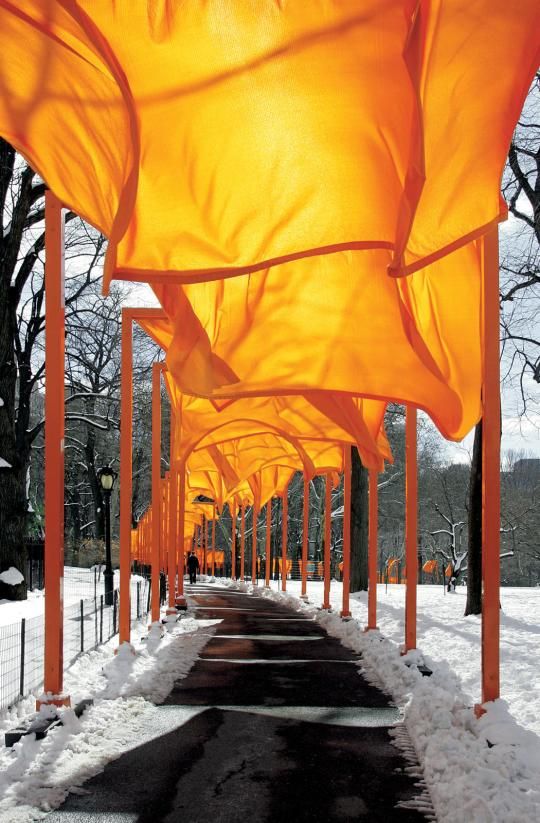 an outdoor walkway covered in snow next to tall orange poles with large drapes hanging from them