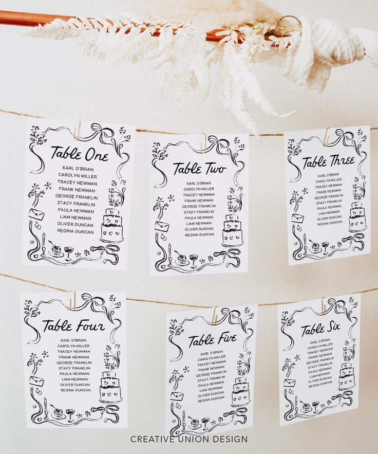 wedding seating cards hanging on a rope in front of a white backdrop with black and white designs