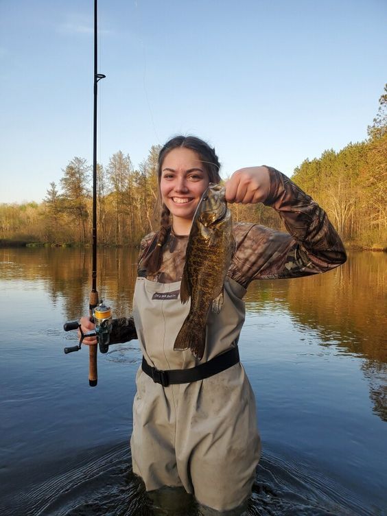 a woman holding a fish in her hands while standing in the water with a fishing rod