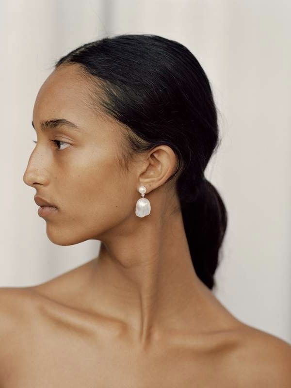 a woman in a white dress with earrings on her head looking off to the side