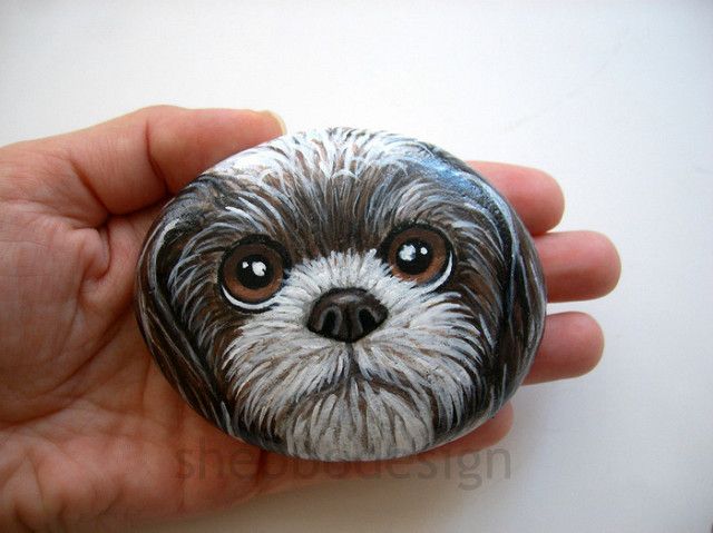 a hand holding a painted rock with a small dog's face on the front