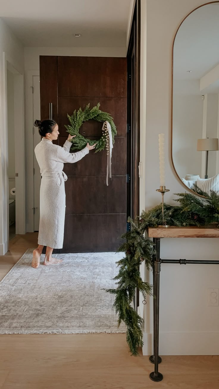 a woman in a bathrobe is placing a wreath on the front door handle