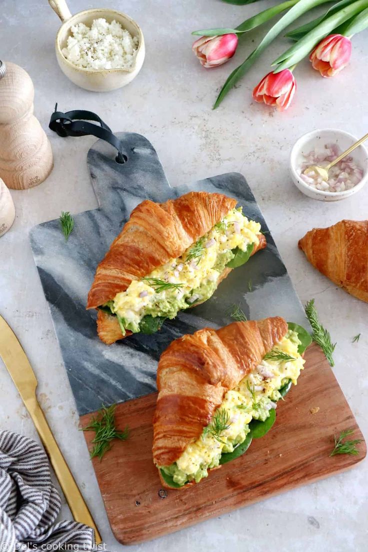 two croissants are cut in half on a cutting board next to flowers