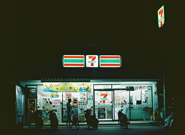 several people are standing in front of a convenience store at night with their backs to the camera