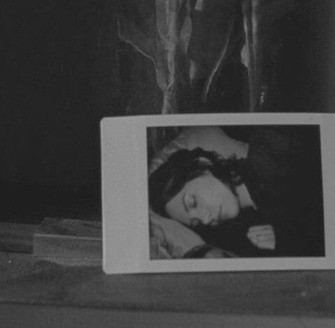 a black and white photo of a woman laying on a bed next to a vase with flowers in it