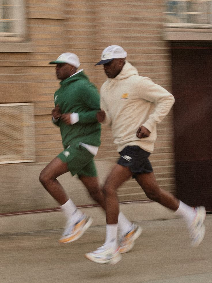 two men are running down the street in green and white outfits, one is wearing a hat