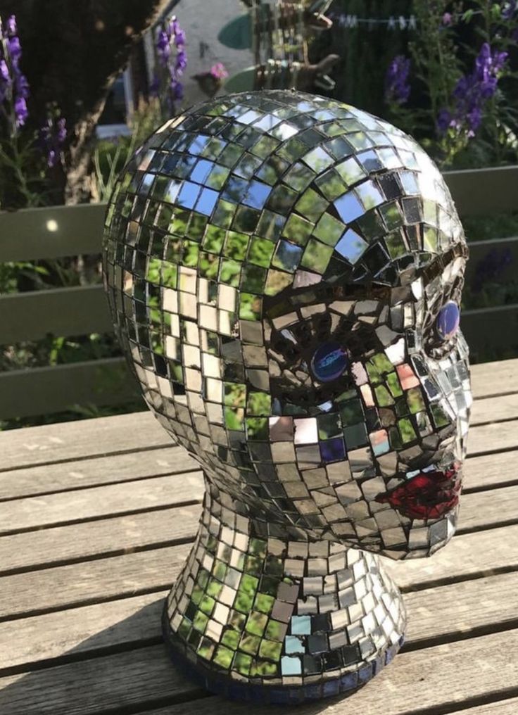 a mosaic head sitting on top of a wooden table next to purple and white flowers