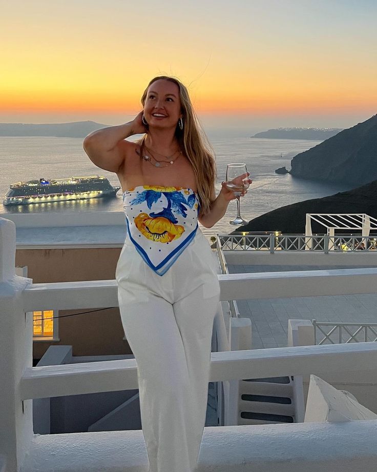 a woman standing on top of a roof next to the ocean holding a glass of wine