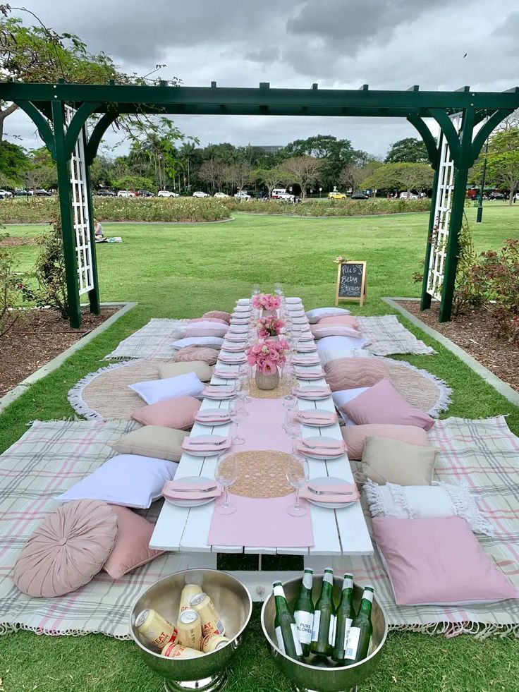 a picnic table set up with pink and white plates, napkins and wine bottles