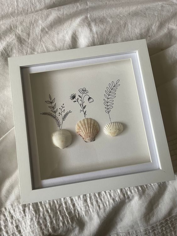 three seashells in a shadow box frame on a white bed with linens